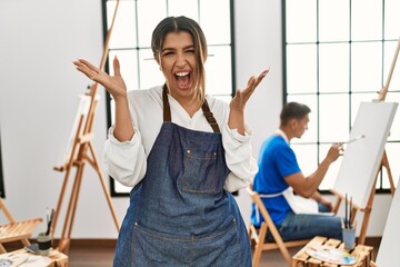 Canvas Print - Young hispanic couple at art studio celebrating victory with happy smile and winner expression with raised hands