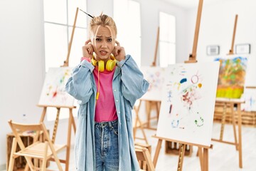 Poster - Young caucasian girl at art studio covering ears with fingers with annoyed expression for the noise of loud music. deaf concept.