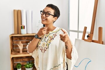 Sticker - Young hispanic woman with short hair at art studio pointing fingers to camera with happy and funny face. good energy and vibes.