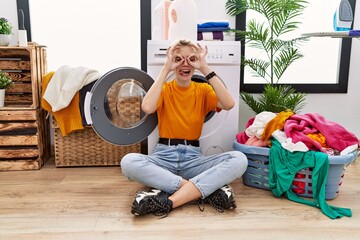 Sticker - Young blonde woman doing laundry sitting by washing machine doing ok gesture like binoculars sticking tongue out, eyes looking through fingers. crazy expression.