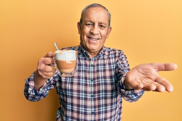 Wall Mural - Handsome senior man with grey hair drinking a cup coffee smiling cheerful offering palm hand giving assistance and acceptance.