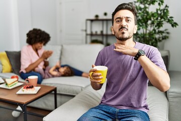 Canvas Print - Hispanic father of interracial family drinking a cup coffee cutting throat with hand as knife, threaten aggression with furious violence