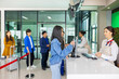 © shine - Different ages and nationalities passengers standing in queue to check in at airport terminal. Young asian woman showing flight ticket to staff on phone and waiting for her boarding pass...