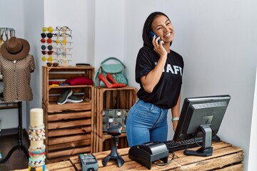 Poster - Young latin woman talking on the smartphone working at clothing store