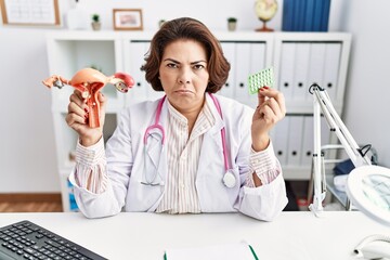 Poster - Middle age hispanic doctor woman holding anatomical female genital organ and birth control pills depressed and worry for distress, crying angry and afraid. sad expression.