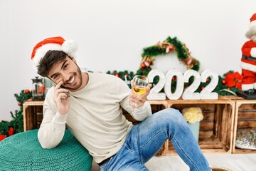 Poster - Young hispanic man smiling happy wearing christmas hat talking on the smartphone celebrating 2022 new year at home.