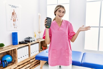 Sticker - Young physiotherapist woman working at pain recovery clinic holding dataphone celebrating achievement with happy smile and winner expression with raised hand