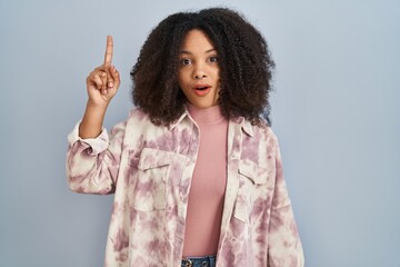 Wall Mural - Young african american woman standing over blue background pointing finger up with successful idea. exited and happy. number one.