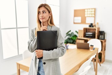 Sticker - Blonde business woman at the office thinking concentrated about doubt with finger on chin and looking up wondering