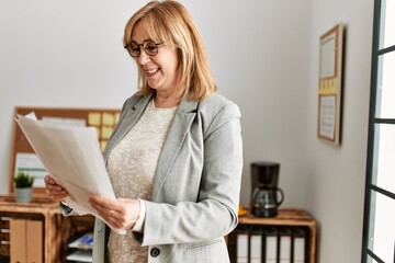 Wall Mural - Middle age businesswoman smiling happy holding paperwork standing at the office.