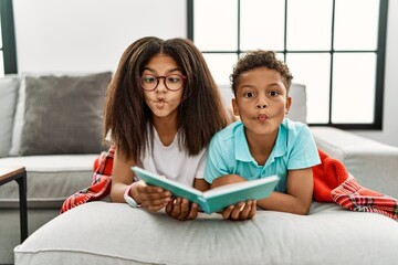 Wall Mural - Two siblings lying on the sofa reading a book making fish face with lips, crazy and comical gesture. funny expression.