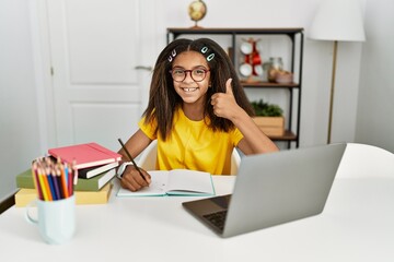 Poster - Young african american girl doing homework at home doing happy thumbs up gesture with hand. approving expression looking at the camera showing success.