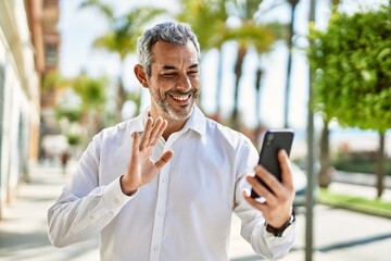 Sticker - Middle age grey-haired man doing video call using smartphone at the city.