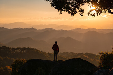 Young hiker man standing on top of mountain with the sun in the sunset