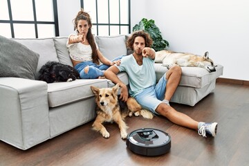 Sticker - Young hispanic couple relaxing at home by vacuum robot pointing with finger to the camera and to you, confident gesture looking serious