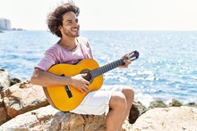 Young Hispanic Man Playing Classical Guitar Sitting On Rock At The Beach.