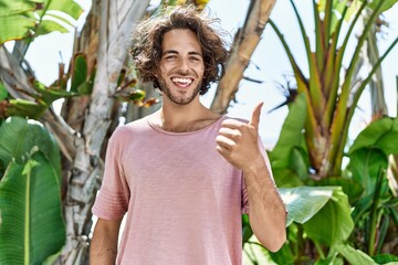 Wall Mural - Young hispanic man outdoors on a sunny day smiling happy and positive, thumb up doing excellent and approval sign