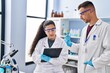 © Krakenimages.com - Man and woman wearing scientist uniform write on clipboard holding test tube at laboratory