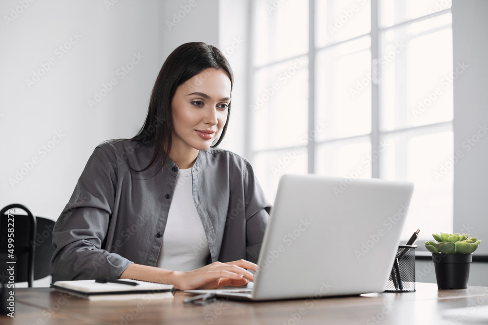 Young woman using laptop computer at office. Student girl working at home. Online work or study, freelance, business, office lifestyle concept.