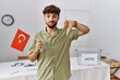 Young arab man at political campaign election holding turkey flag with angry face, negative sign showing dislike with thumbs down, rejection concept