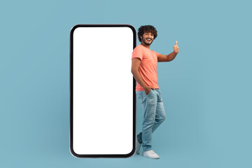 Wall Mural - Happy indian man posing by big smartphone, showing thumb up