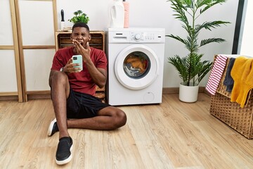 Canvas Print - Young african american man using smartphone waiting for washing machine bored yawning tired covering mouth with hand. restless and sleepiness.