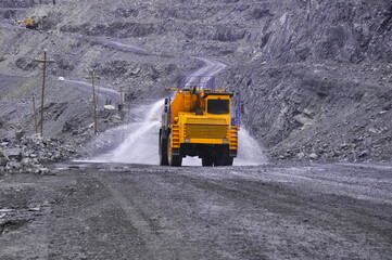 Wall Mural - Heavy truck pours the road with water in the iron ore quarry. Dust removal, protection of the environment. Irrigation of the road from dust