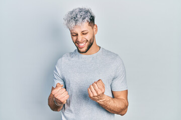 Young hispanic man with modern dyed hair wearing casual grey t shirt excited for success with arms raised and eyes closed celebrating victory smiling. winner concept.