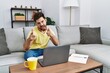 © Krakenimages.com - Young man with beard using laptop at home pointing fingers to camera with happy and funny face. good energy and vibes.