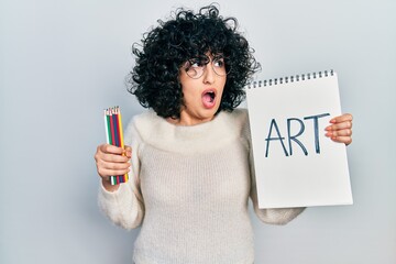 Sticker - Young middle east woman holding art notebook angry and mad screaming frustrated and furious, shouting with anger. rage and aggressive concept.