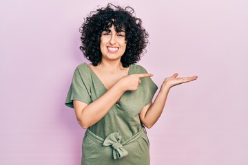 Sticker - Young middle east woman wearing casual clothes amazed and smiling to the camera while presenting with hand and pointing with finger.