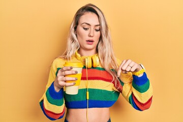 Sticker - Beautiful young blonde woman drinking cup of coffee wearing headphones pointing down with fingers showing advertisement, surprised face and open mouth