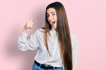 Young brunette teenager wearing business white shirt smiling doing phone gesture with hand and fingers like talking on the telephone. communicating concepts.