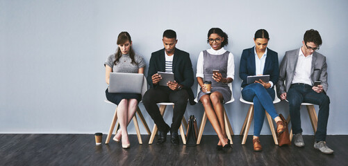 Fototapete - These seats are for those on the shortlist. Full length shot of a group of young businesspeople waiting in line for their interviews.