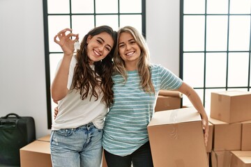 Wall Mural - Young beautiful couple smiling happy holding cardboard box and key of new home.