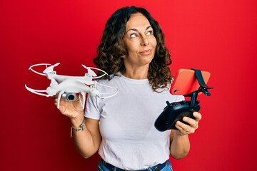 Sticker - Middle age hispanic woman using drone smiling looking to the side and staring away thinking.