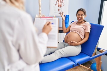 Sticker - Young pregnant woman at physiotherapist clinic in shock face, looking skeptical and sarcastic, surprised with open mouth