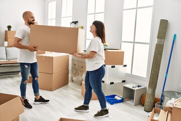 Wall Mural - Young hispanic couple smiling happy holding big cardboard box at new home.