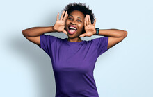 African American Woman With Afro Hair Wearing Casual Purple T Shirt Smiling Cheerful Playing Peek A Boo With Hands Showing Face. Surprised And Exited