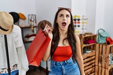 Young Brunette Woman Holding Shopping Bags At Retail Shop Angry And Mad Screaming Frustrated And Furious, Shouting With Anger. Rage And Aggressive Concept.