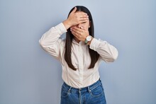 Young Latin Woman Standing Over Blue Background Covering Eyes And Mouth With Hands, Surprised And Shocked. Hiding Emotion