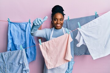 Poster - African american woman with braided hair washing clothes at clothesline approving doing positive gesture with hand, thumbs up smiling and happy for success. winner gesture.