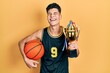 © Krakenimages.com - Young hispanic man wearing basketball uniform holding ball and prize smiling and laughing hard out loud because funny crazy joke.