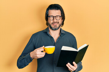 Wall Mural - Middle age caucasian man reading book drinking cup of tea clueless and confused expression. doubt concept.