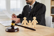 © Studio Romantic - Gavel and little wooden figures of husband, wife and child up close on table in courthouse, and judge reading divorce settlement in background. Family law, court trial, parent getting custody concept