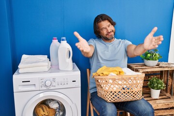 Wall Mural - Handsome middle age man waiting for laundry looking at the camera smiling with open arms for hug. cheerful expression embracing happiness.