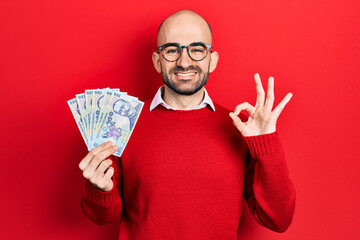 Sticker - Young bald man holding 100 romanian leu banknotes doing ok sign with fingers, smiling friendly gesturing excellent symbol