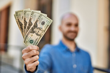 Poster - Young hispanic man smiling happy holding dollars at the city.