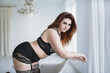 Chubby redhead plus size woman model posing in black lace lingerie in white bedroom
