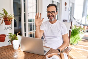 Sticker - Middle age man using computer laptop at home waiving saying hello happy and smiling, friendly welcome gesture